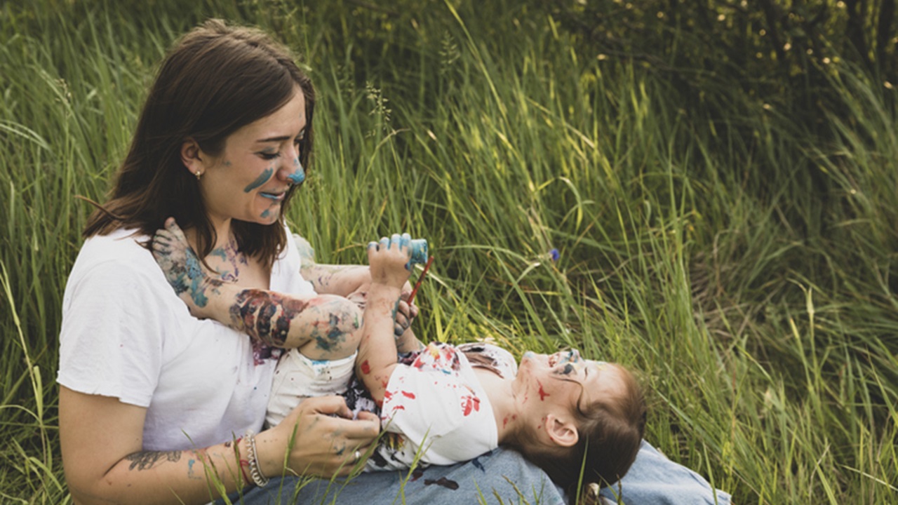Lachende Mutter und Kind mit Farben bemalt sitzen in Wiese