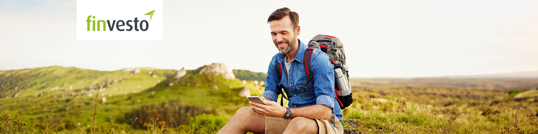 Mann mit Rucksack auf Berg sitzend schaut auf Smartphone